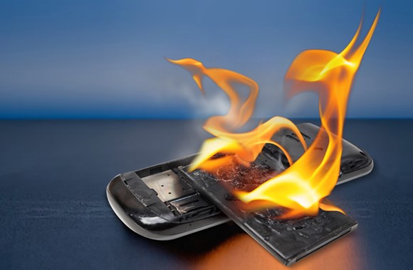 Brennender Handy-Akku auf vor Blau-Grauem Hintergrund.