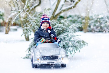 Kleiner Junge fährt in einer Winterlandschaft im Spielzeugauto und transportiert einen Baum