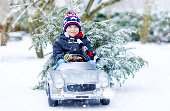 Kleiner Junge fährt in einer Winterlandschaft im Spielzeugauto und transportiert einen Baum