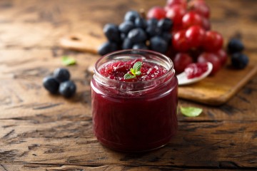 Marmeladenglas steht auf Holz vor verschiedenen Beeren.