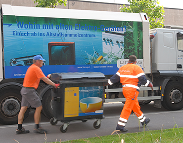 Zwei Müllmänner ziehen eine Mülltonne vor einem Müllabfuhrwagen von LINZ AG ABFALL