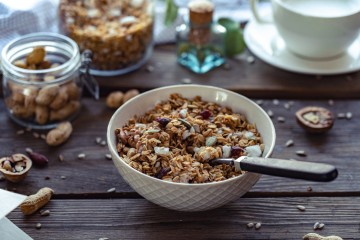 Müsli in einer Schale auf Holztisch. Im Hintergrund befinden sich Nüsse und andere Müslisorten