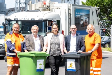 fünf Personen stehen vor einem Restmüll und Bioabfall Tonne, dahinter eine Müllfahrzeug