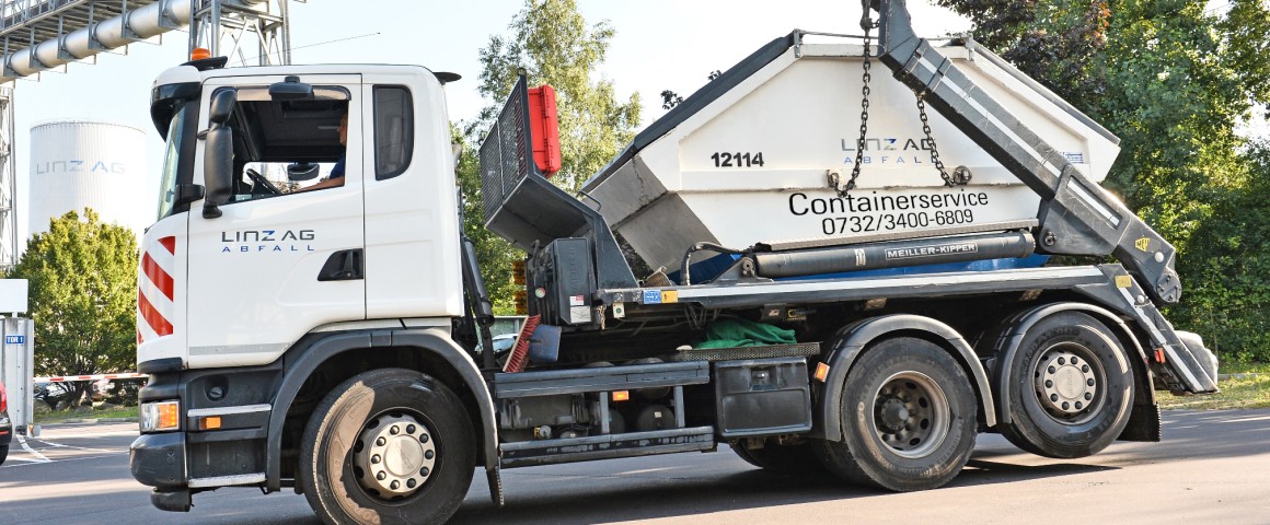 Ein Lastkraftwagen hat einen Abfallcontainer für den Containerverleih von LINZ AG ABFALL aufgeladen.