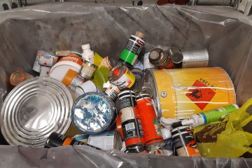 Verschiedene Lackdosen in einem Müllcontainer.