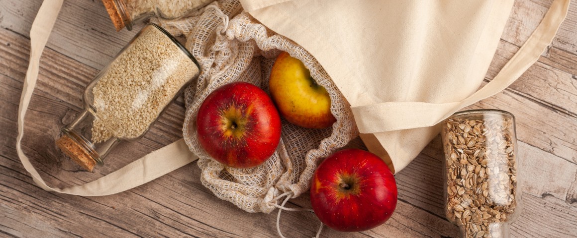 Stofftasche auf Holzboden mit Äpfeln und Körnern.