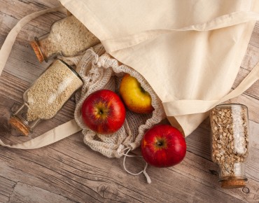 Stofftasche auf Holzboden mit Äpfeln und Körnern.