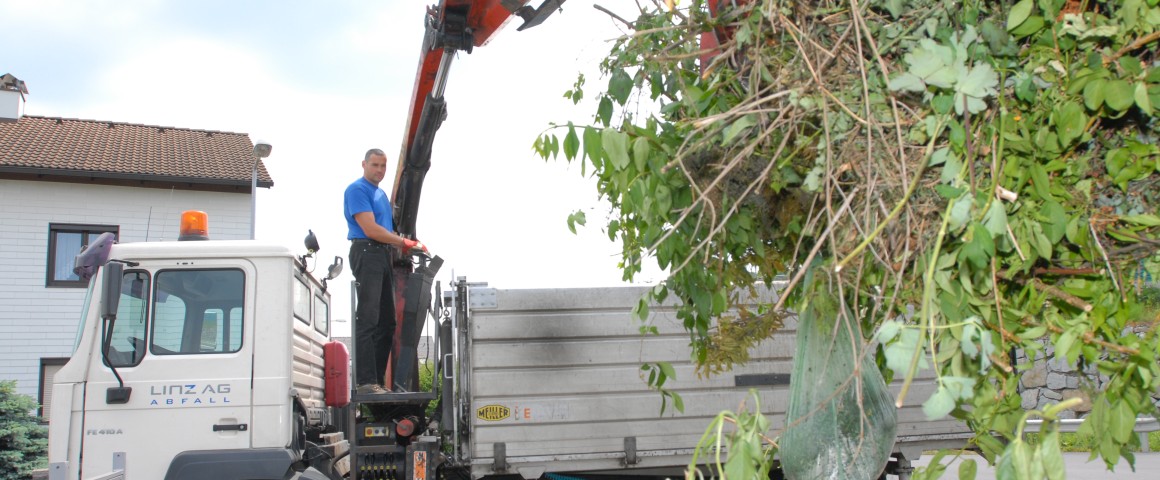 Ein Mitarbeiter von LINZ AG ABFALL hebt mit einem Kran Grünschnitt und Gartenabfälle in einen Container