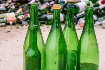 Abbildung von fünf grünen Altglas-Flaschen, vor einem Müllberg.