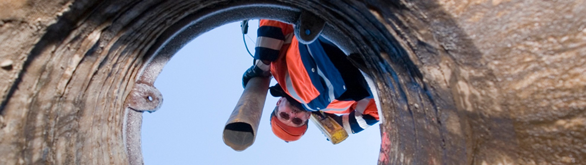 ein Kanalarbeiter schaut von oben in den Kanal hinunter mit dem Schlauch in der Hand