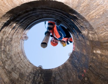 ein Kanalarbeiter schaut von oben in den Kanal hinunter mit dem Schlauch in der Hand