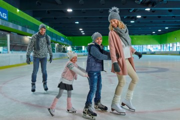 Mutter fährt ganz vorne, Sohn und Tochter hängen sich an sie. Der Vater fährt etwas weiter hinten mit den Eislaufschuhen.