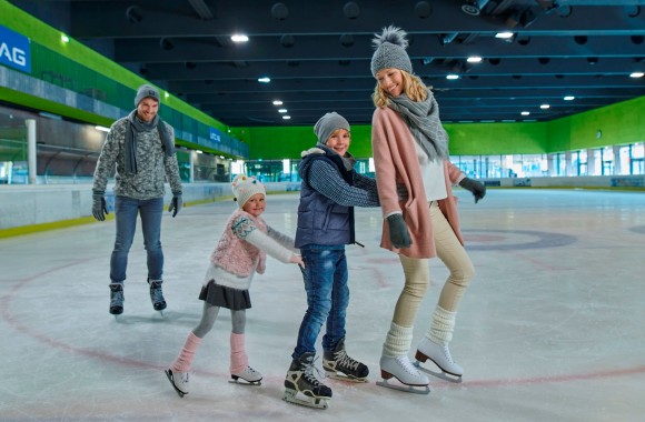 Mutter fährt ganz vorne, Sohn und Tochter hängen sich an sie. Der Vater fährt etwas weiter hinten mit den Eislaufschuhen.