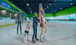 Mutter fährt ganz vorne, Sohn und Tochter hängen sich an sie. Der Vater fährt etwas weiter hinten mit den Eislaufschuhen.