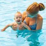 Mutter hält ihr baby ins wasser um ihm das schwimmen zu lernen