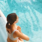 Eine Frau sitzt im Schwimmbecken am Beckenrand und macht eine Yogapose.