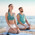 Zwei Personen sitzen auf einer Fitnessmatte am Strand, am Meer.