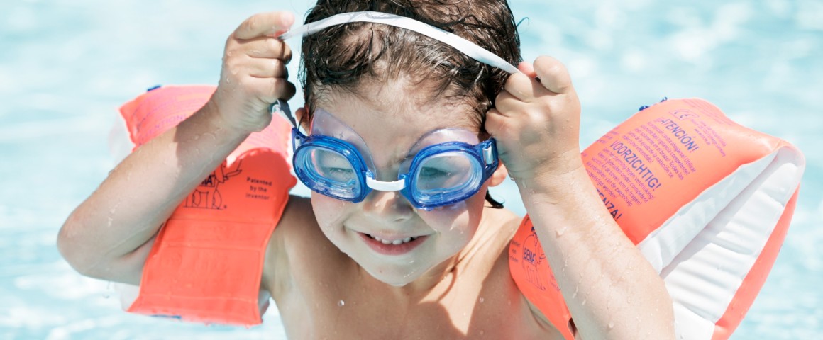 Kleiner Junge mit Schwimmflügeln und Taucherbrille in Pool