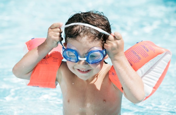 Kleiner Junge mit Schwimmflügeln und Taucherbrille in Pool