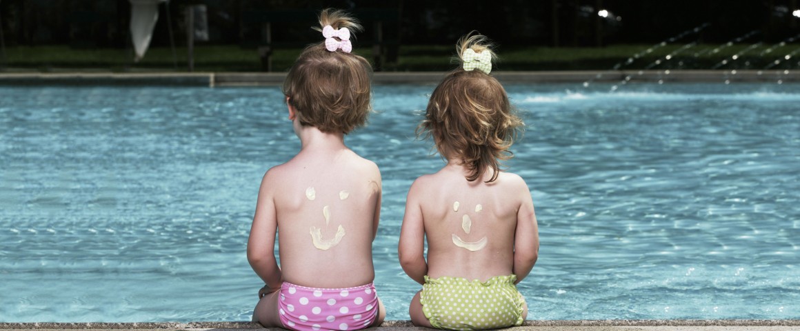 Zwei kleine Mädchen sitzen in bunten Badehosen am Pool