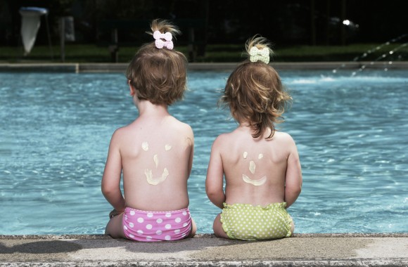 Zwei kleine Mädchen sitzen in bunten Badehosen am Pool