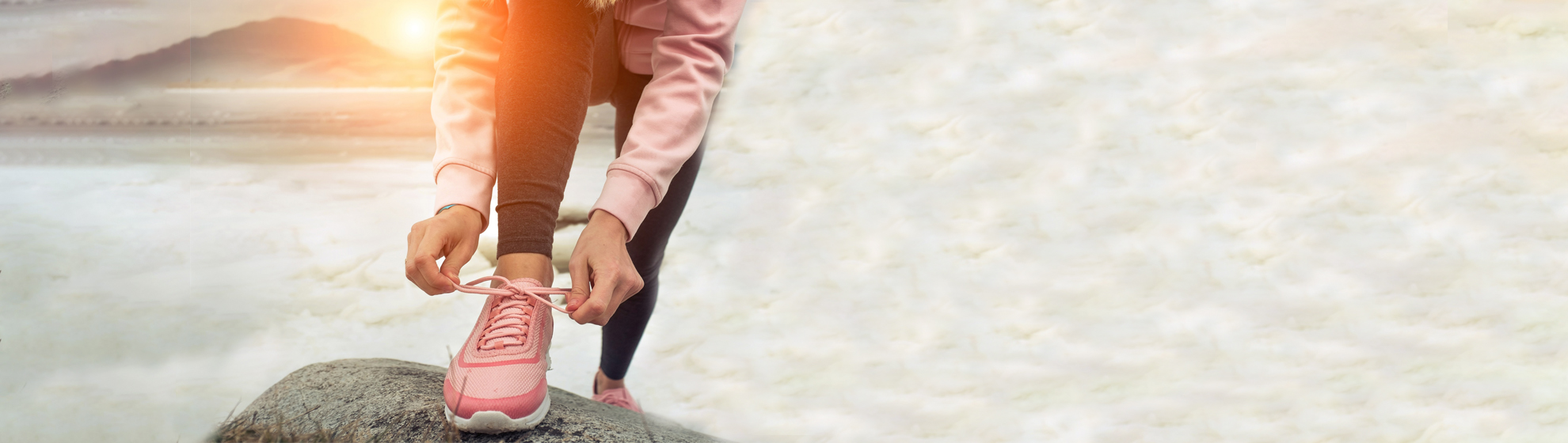 Frau steht im Trainingsoutfi mit dem Rücken zum See und bindet sich die Sportschuhe