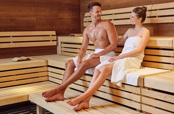 Ein junges Pärchen sitzt in der Sauna und lächtelt sich an.