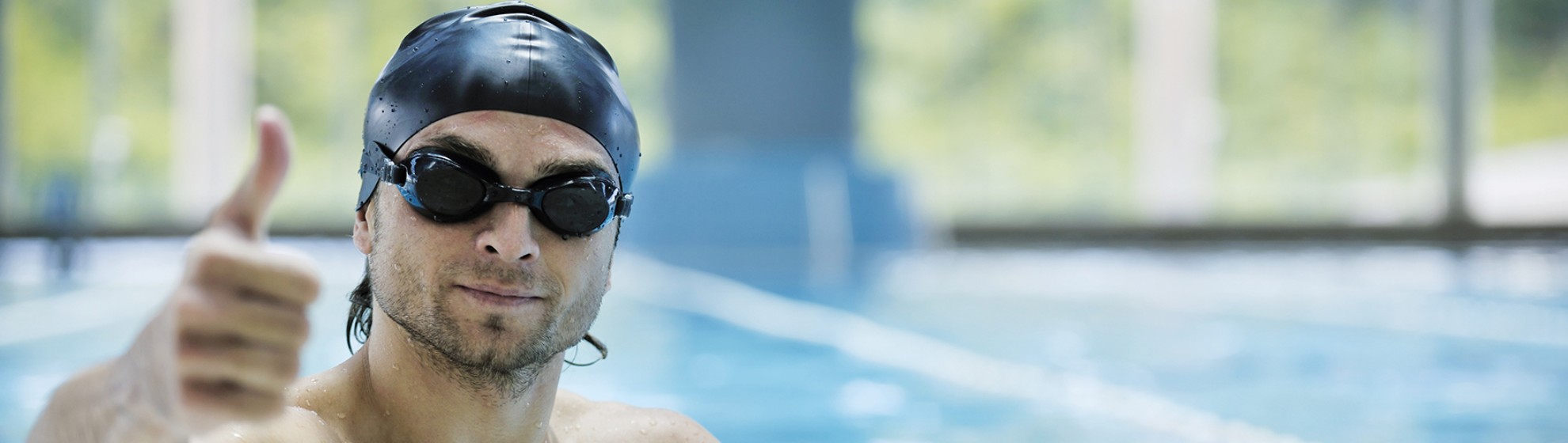 Mann mit Taucherbrille und Badehaube, der den Daumen hochhält, im Schwimmbecken