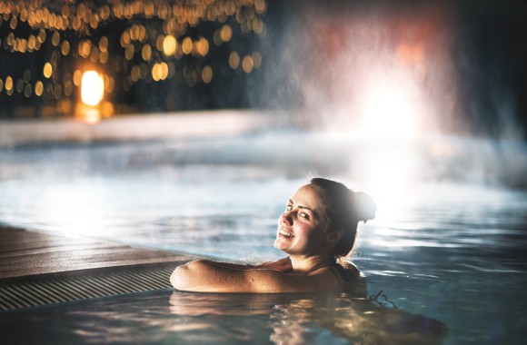 Eine Frau lehnt in der Nacht am Beckenrand eines Schwimmbeckens.