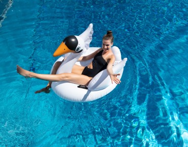 Frau sitzt auf aufgeblasenem Schwan im Schwimmbecken.