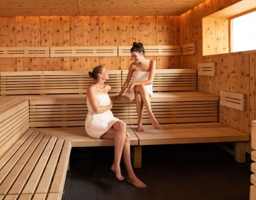 Zwei Frauen sitzen in Sauna und unterhalten sich.