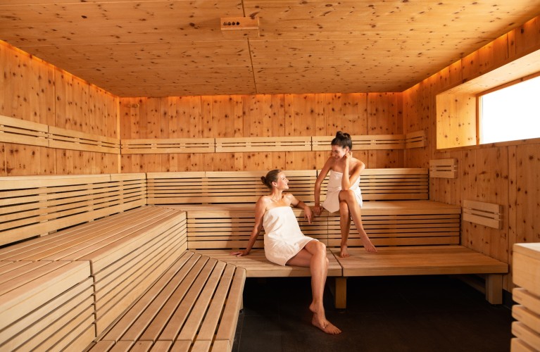 Zwei Frauen sitzen in Sauna und unterhalten sich.