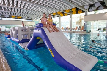 Bild aus der Vogelperspektive aufgenommen. Schwimmbecken in dem sich ein Wasserparcourpark aufgebaut ist. Kinder Klettern auf dem Parcour.