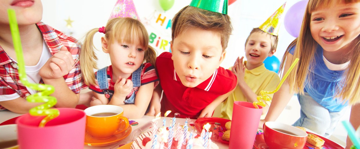 Kinder feiern und Junge bläst Geburtstagskerzen aus