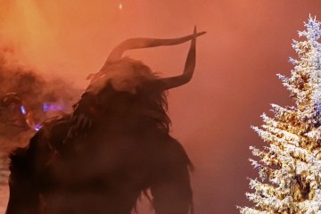 Umriss eines Perchten im Nebel, rechts im Bild ein eingeschneiter Tannenbaum