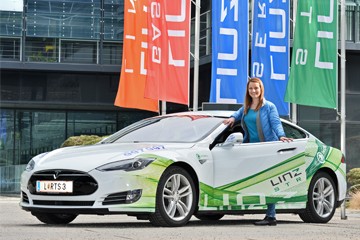 Eine Frau posiert mit einem E-Auto mit LINZ AG-Branding, einem Tesla, vor der LINZ AG
