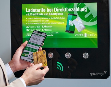 Frau steht mit Ladekarte in der Hand vor der Ladestation.