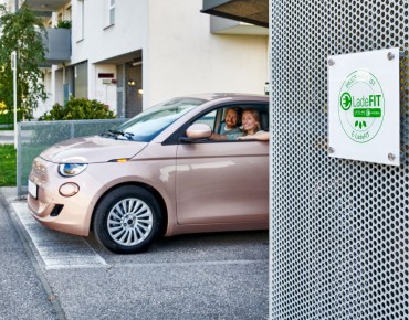 Haus mit Schild "E-LadeFit", dahinter ein Paar im Auto.