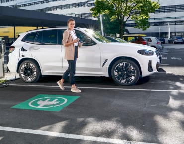 Dame vor weißem Auto neben einer Ladesäule.