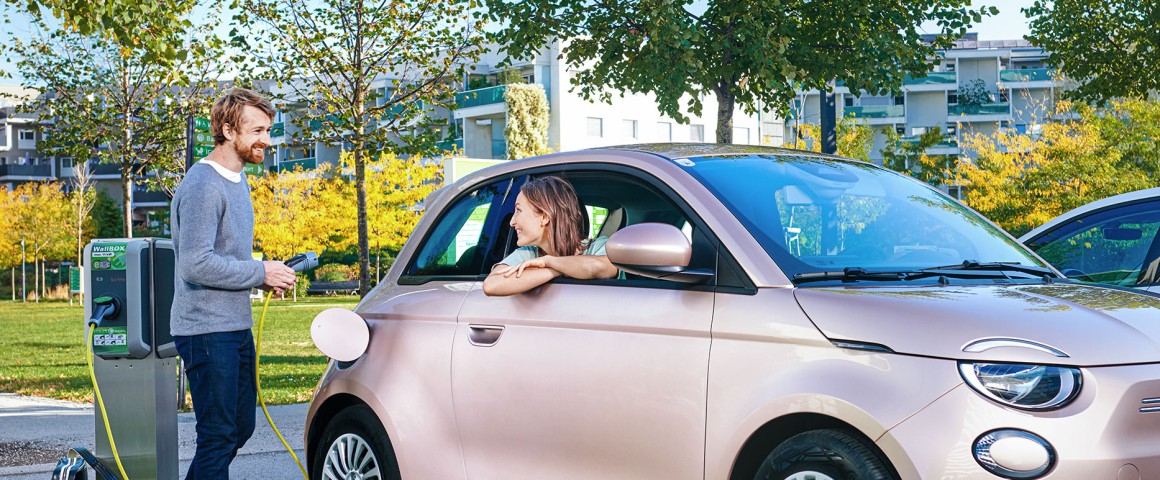 Herr lädt das Auto, Dame sitzt darin.