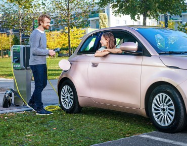 Herr lädt das Auto, Dame sitzt darin.