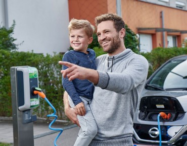 Ein Elektroauto in einer Wohnanlage wird geladen, daneben ein Mann und ein Kind