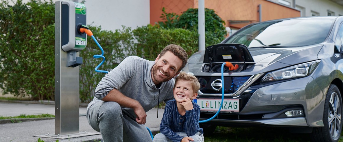 Ein Elektroauto in einer Wohnanlage wird geladen, daneben ein Mann und ein Kind