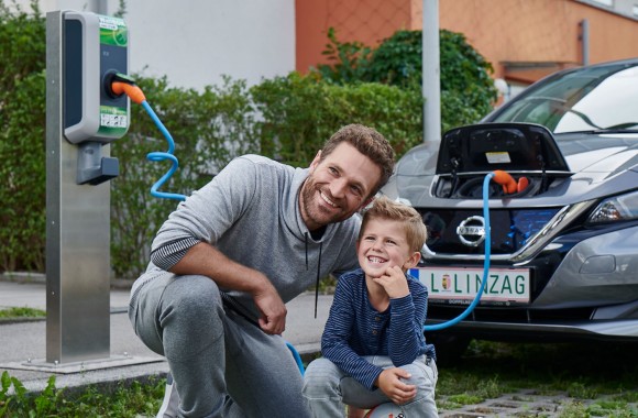 Ein Elektroauto in einer Wohnanlage wird geladen, daneben ein Mann und ein Kind
