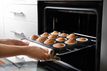 Frau, die ein Blech mit Muffins aus dem Ofen nimmt