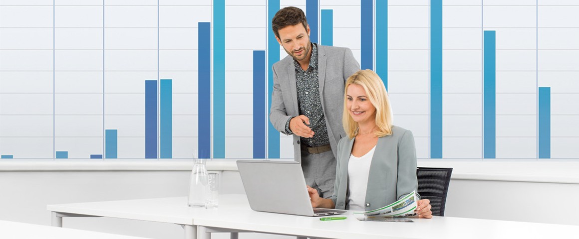 Ein Mann schaut einer Frau beim Arbeiten am Laptop über die Schulter