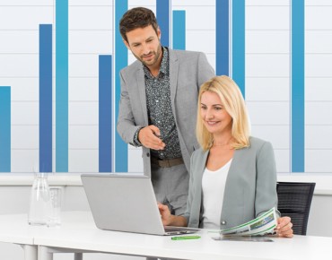 Ein Mann schaut einer Frau beim Arbeiten am Laptop über die Schulter
