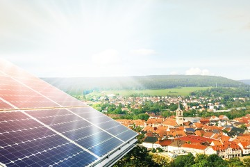 Luftaufnahme einer Gemeinde, im Vordergrund ist eine Photovoltaikfläche zu sehen