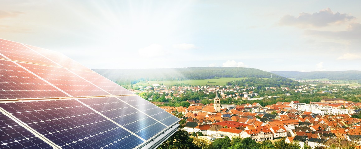 Luftaufnahme einer Gemeinde, im Vordergrund ist eine Photovoltaikfläche zu sehen