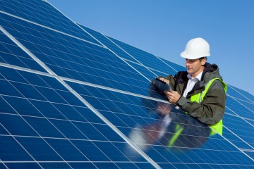 Aufnahme eines Ingenieurs auf einer PV-Anlage, der ein Tablet bedient.